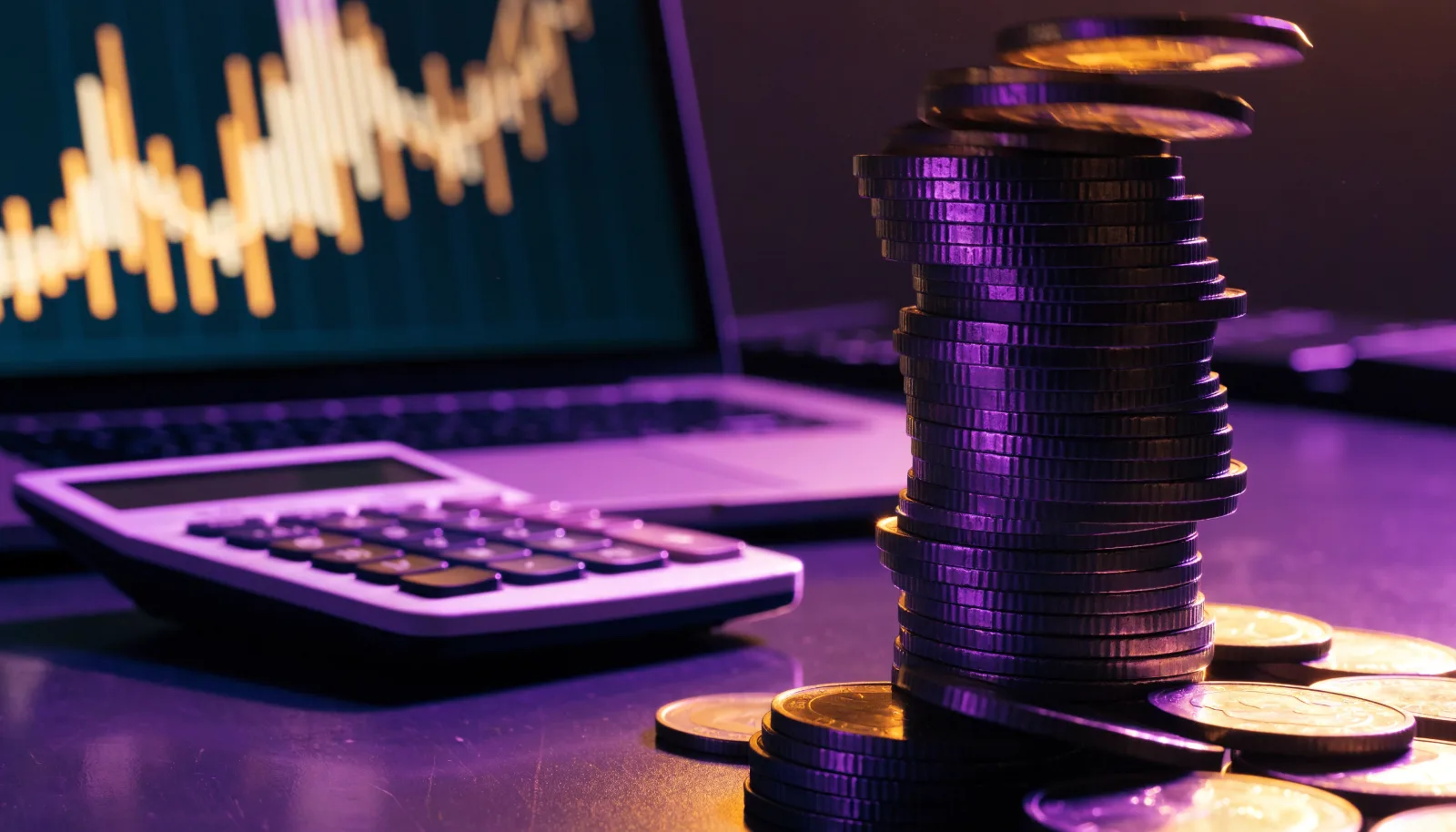 Stack of pound coins and a calculator beside a laptop showing a performance chart